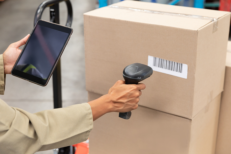 Female worker scanning package with barcode scanner while using digital tablet in freight and distribution warehouse. 